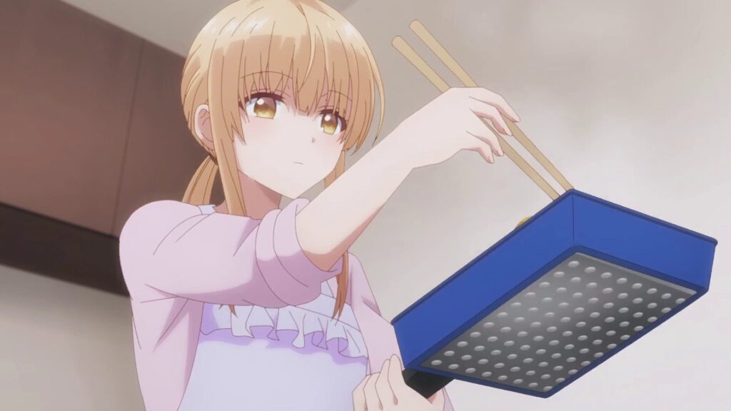 アニメ『お隣の天使様』第2話。エプロン姿で真剣な表情を浮かべ、玉子焼き器で料理を作る椎名真昼のシーン。