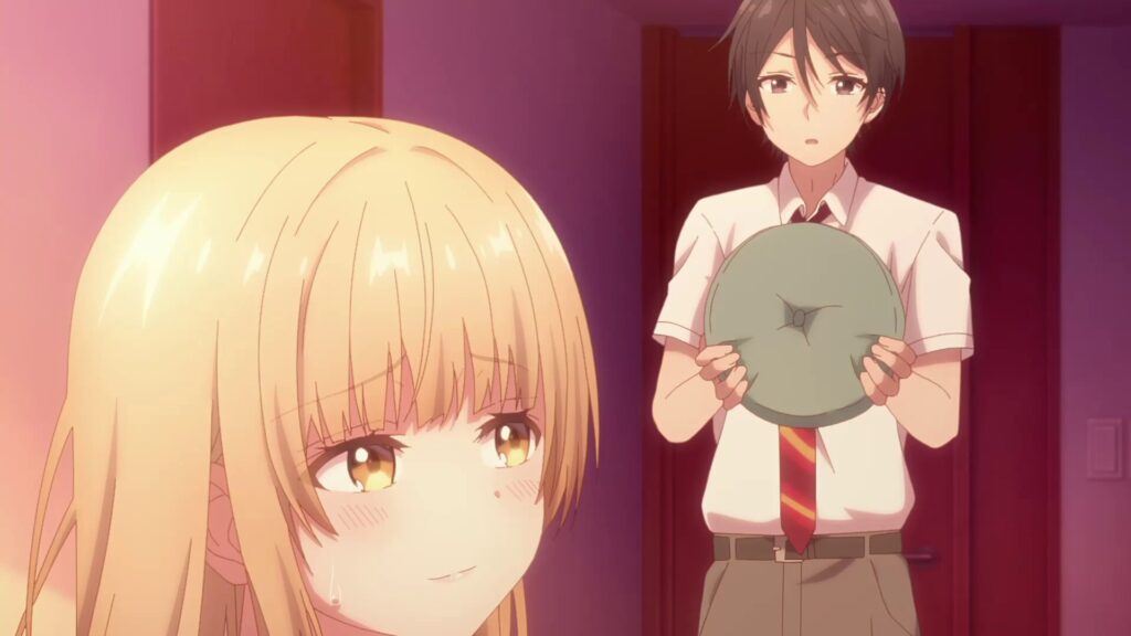 金髪の少女が照れた表情を浮かべ、後ろで男子高校生がクッションを持ちながら驚いた様子を見せているアニメシーン。